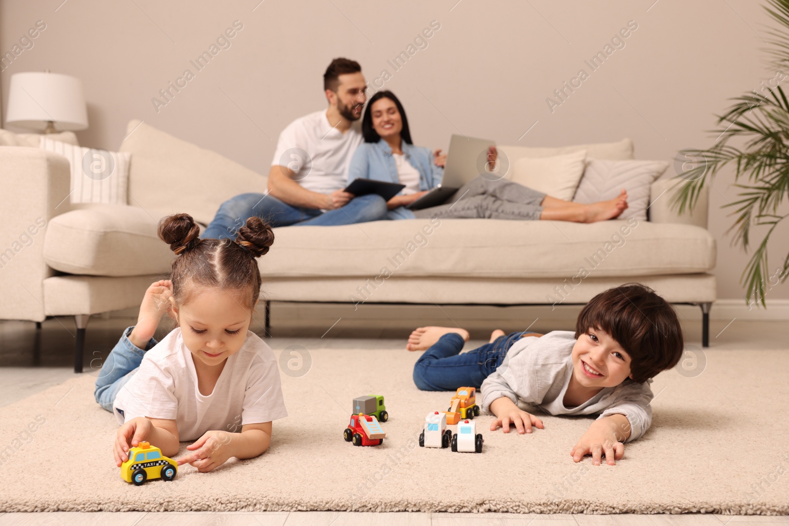 Photo of Cute children playing with toys while parents using gadgets on sofa in living room