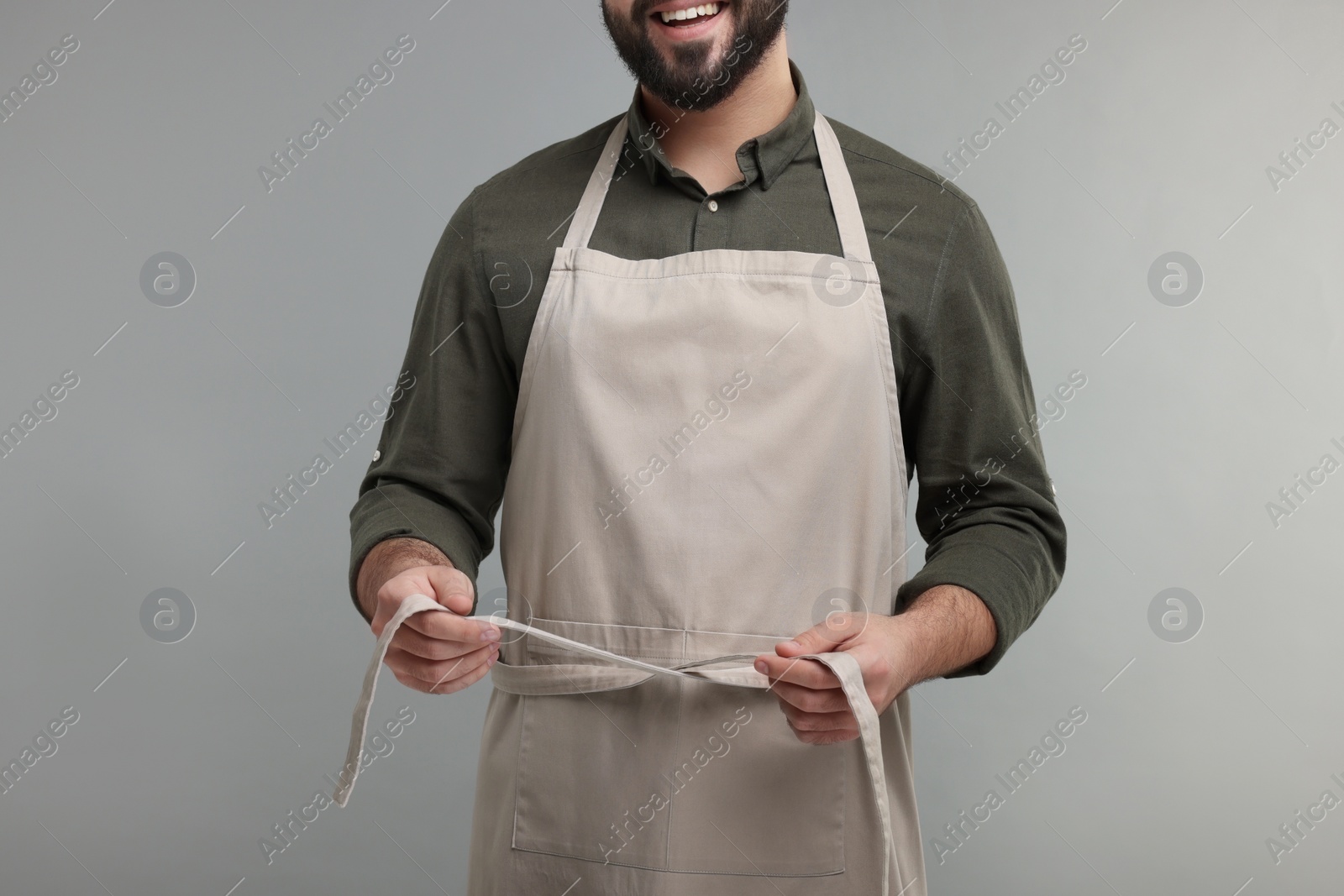 Photo of Smiling man in kitchen apron on grey background, closeup. Mockup for design