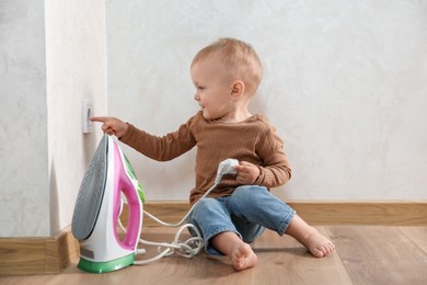 Photo of Little child playing with electrical socket and iron plug at home. Dangerous situation