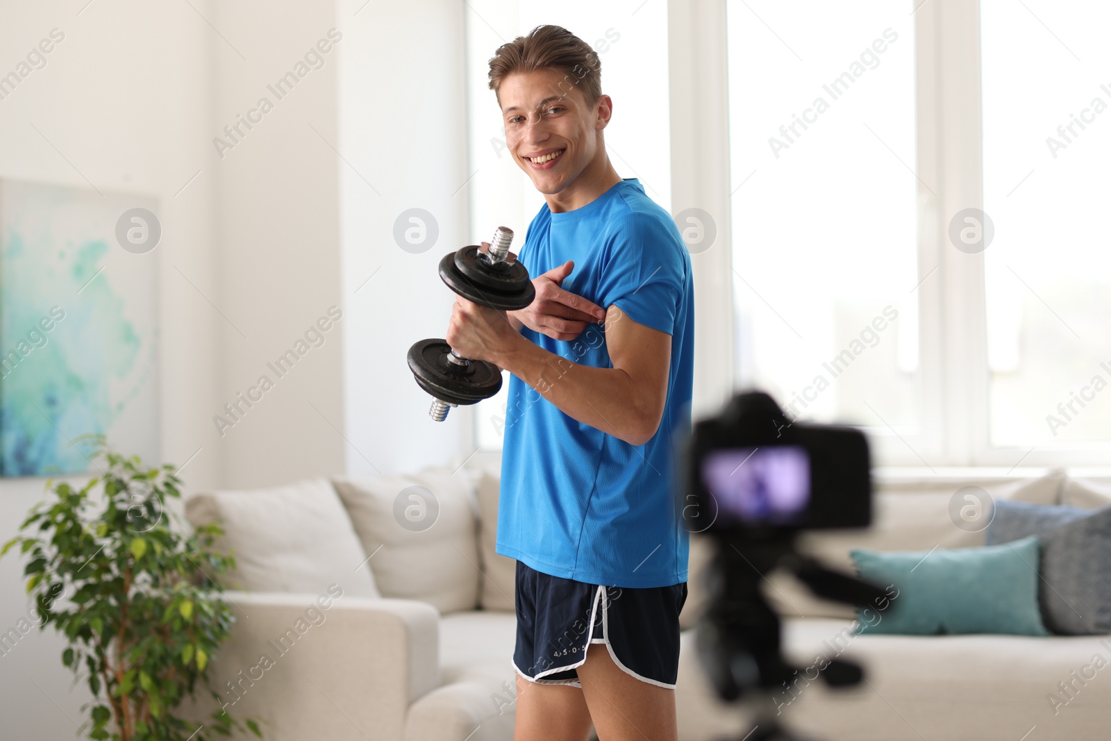 Photo of Smiling sports blogger working out with dumbbell while recording fitness lesson at home