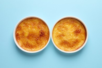 Delicious creme brulee in ramekins on light blue background, flat lay