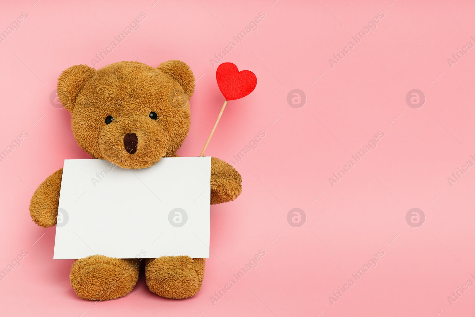 Photo of Cute teddy bear with red heart and blank card on pink background, space for text. Valentine's day celebration