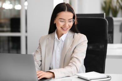 Photo of Happy woman using modern laptop at white desk in office