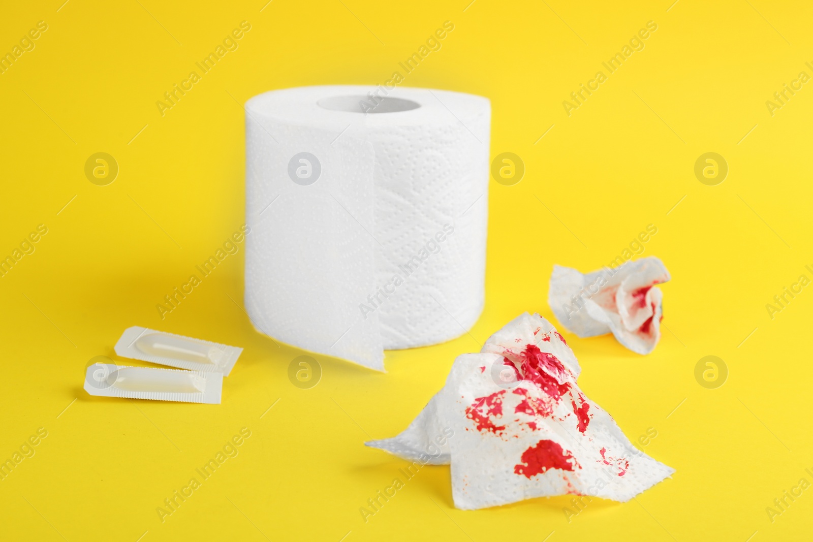 Photo of Sheets of toilet paper with blood and suppositories on yellow background. Hemorrhoid problems