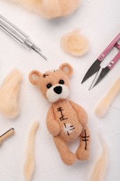 Photo of Felted bear, wool and tools on white table, flat lay