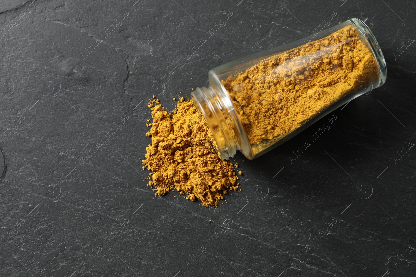 Photo of Jar with dry curry powder on dark textured table, top view. Space for text
