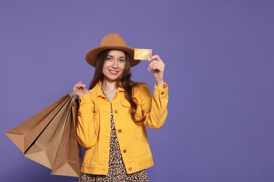Stylish young woman with shopping bags and credit card on purple background, space for text
