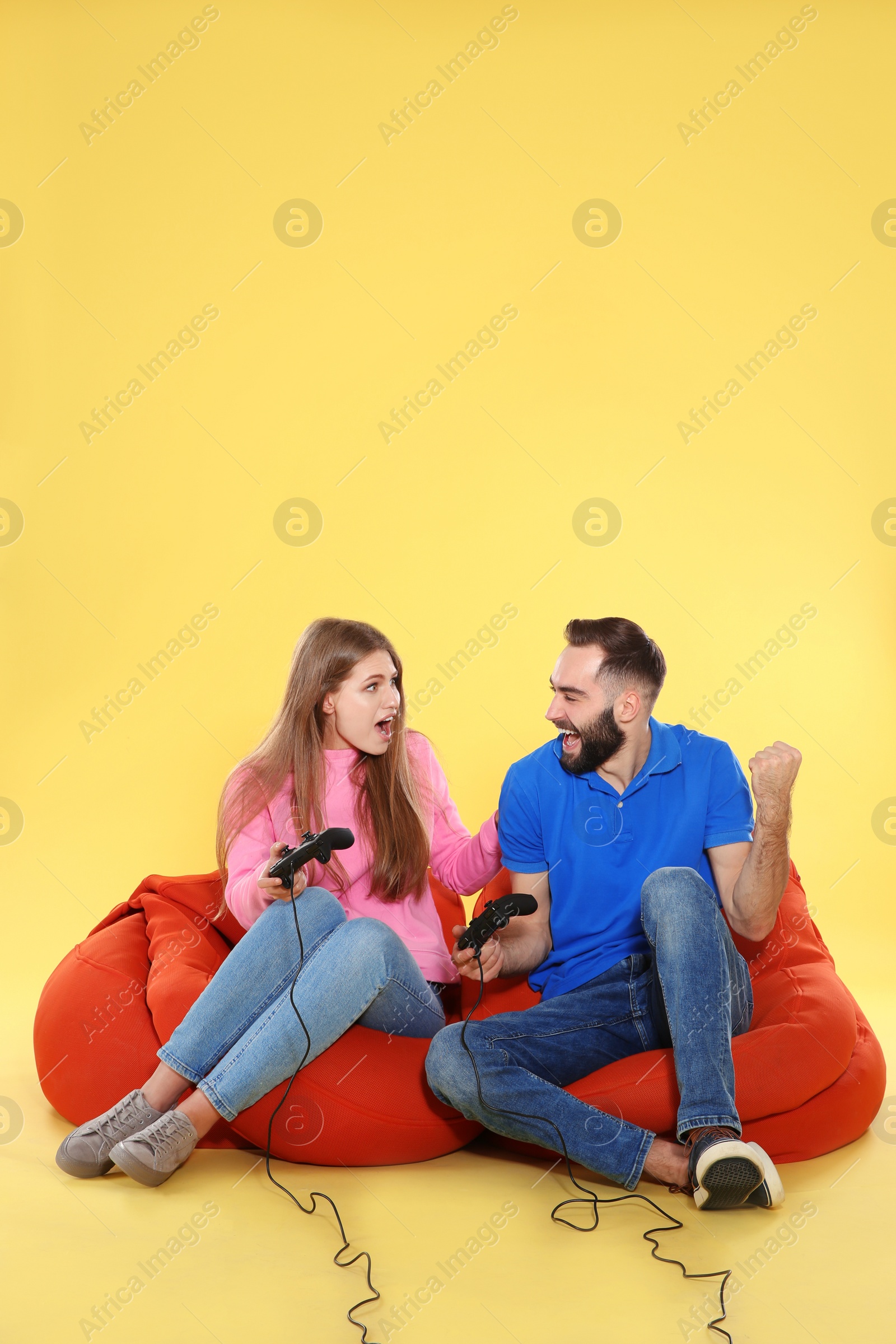 Photo of Emotional couple playing video games with controllers on color background. Space for text