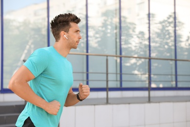 Young sportsman with wireless earphones running on city street