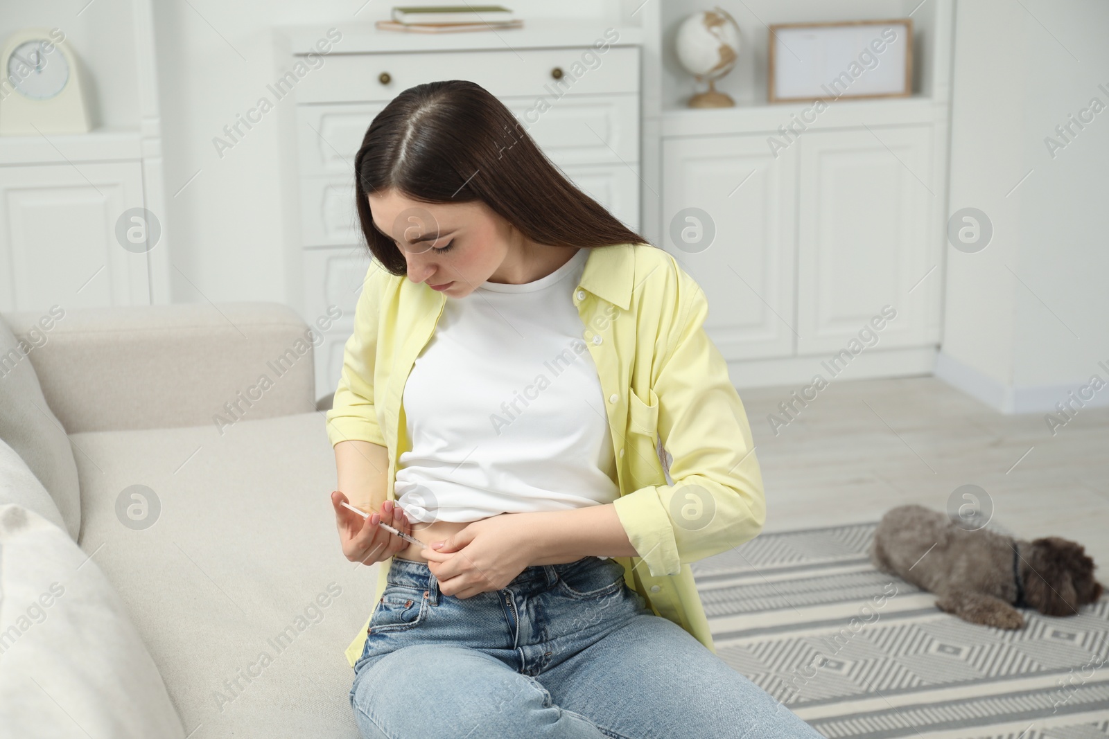 Photo of Diabetes. Woman making insulin injection into her belly on sofa at home