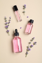 Photo of Bottles of essential oil and lavender flowers on beige background, flat lay