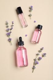 Bottles of essential oil and lavender flowers on beige background, flat lay