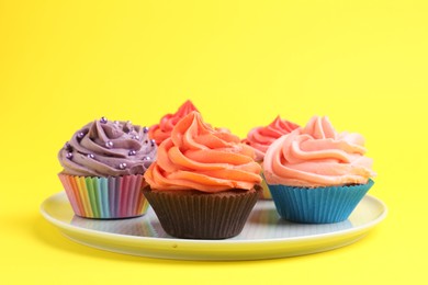 Delicious cupcakes with bright cream on yellow background