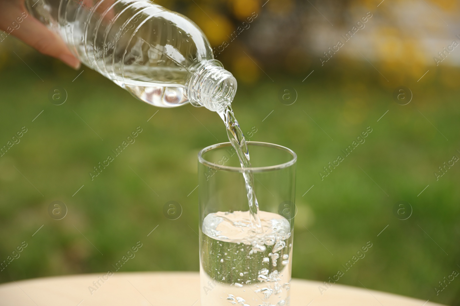 Photo of Woman pouring water from bottle into glass outdoors, closeup