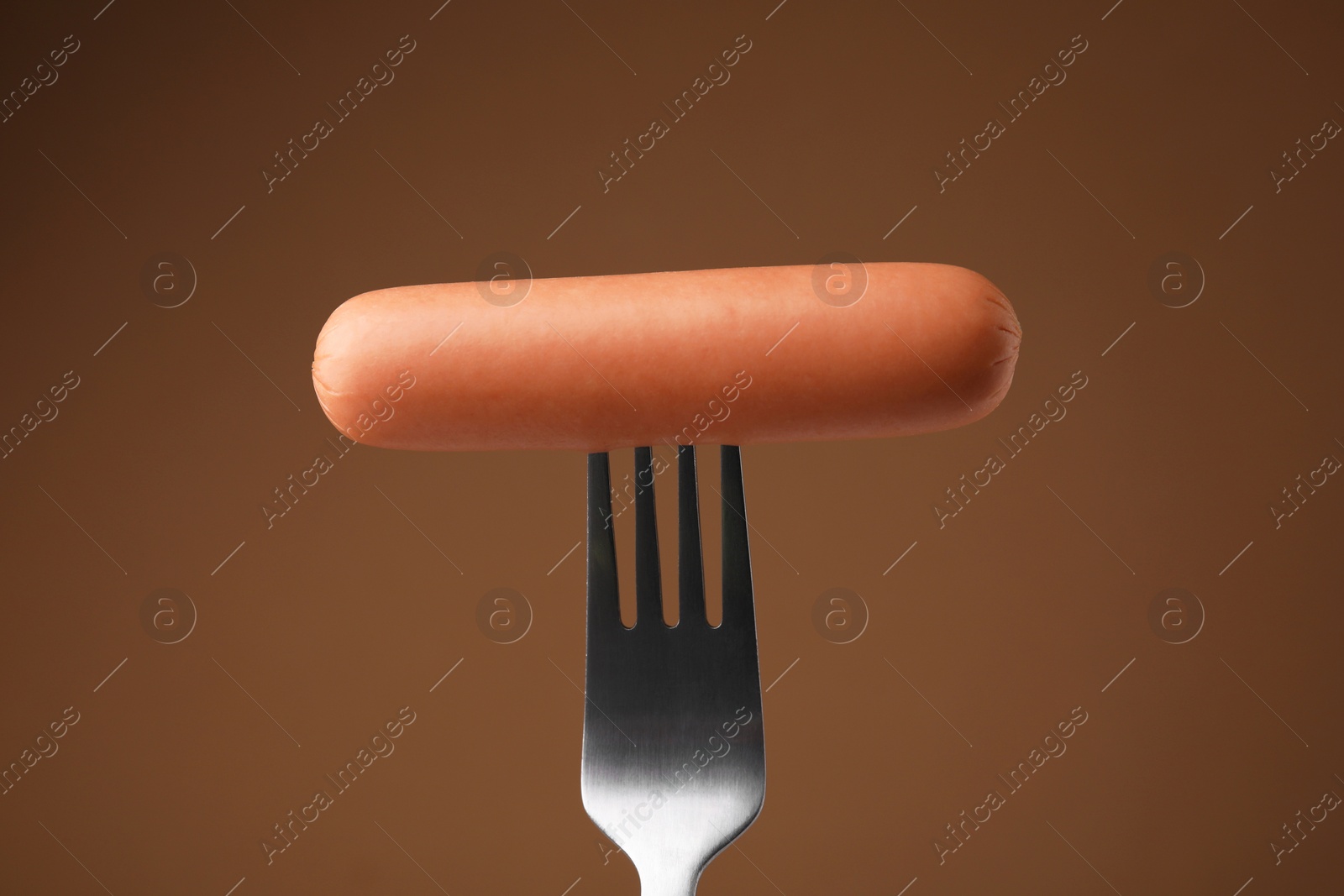 Photo of Delicious boiled sausage on fork against brown background, closeup