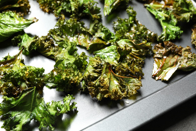 Tasty kale chips with seeds on baking sheet, closeup