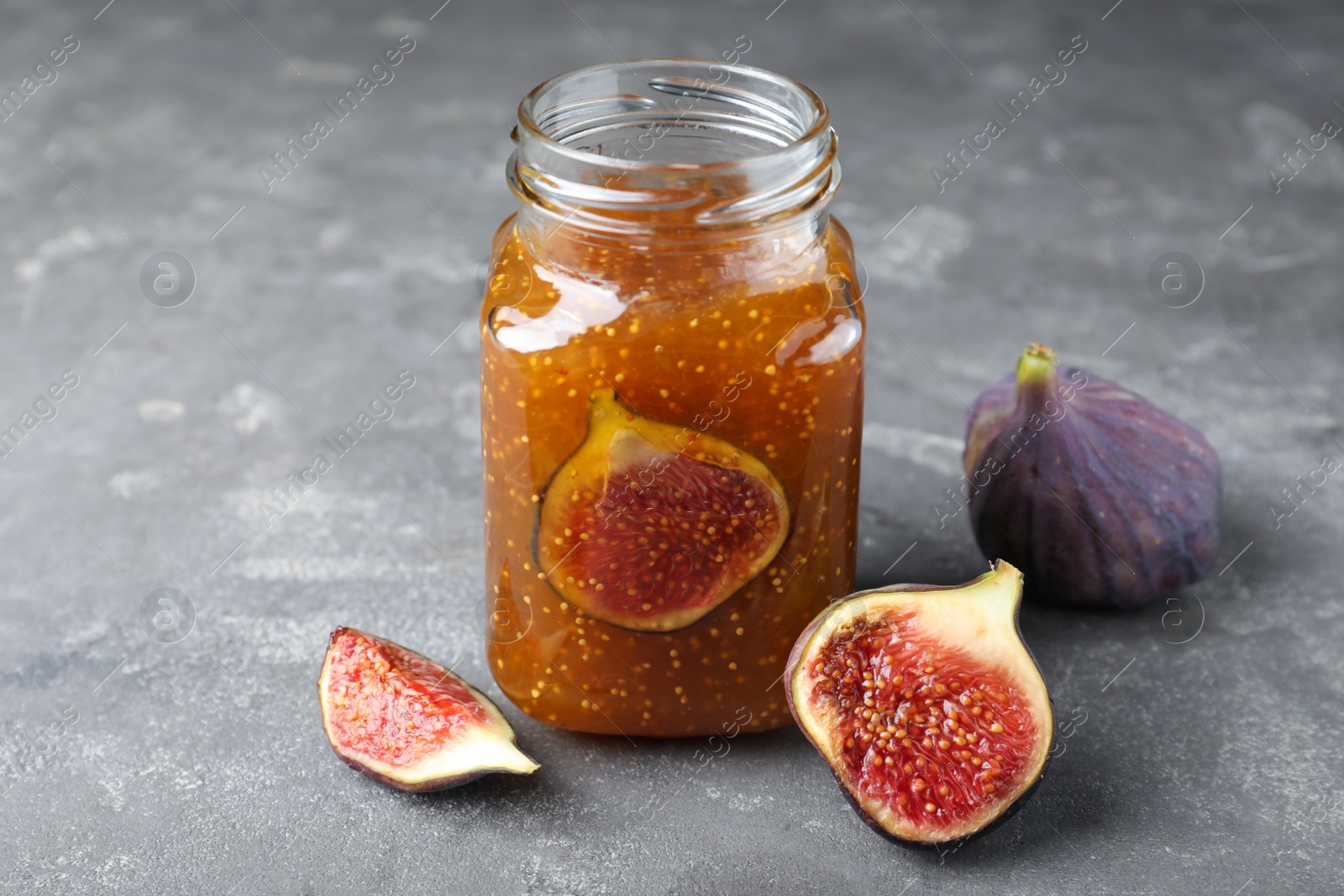 Photo of Delicious fig jam and fresh fruits on grey table