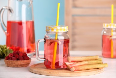 Tasty rhubarb cocktail with raspberry and stalks on white wooden table