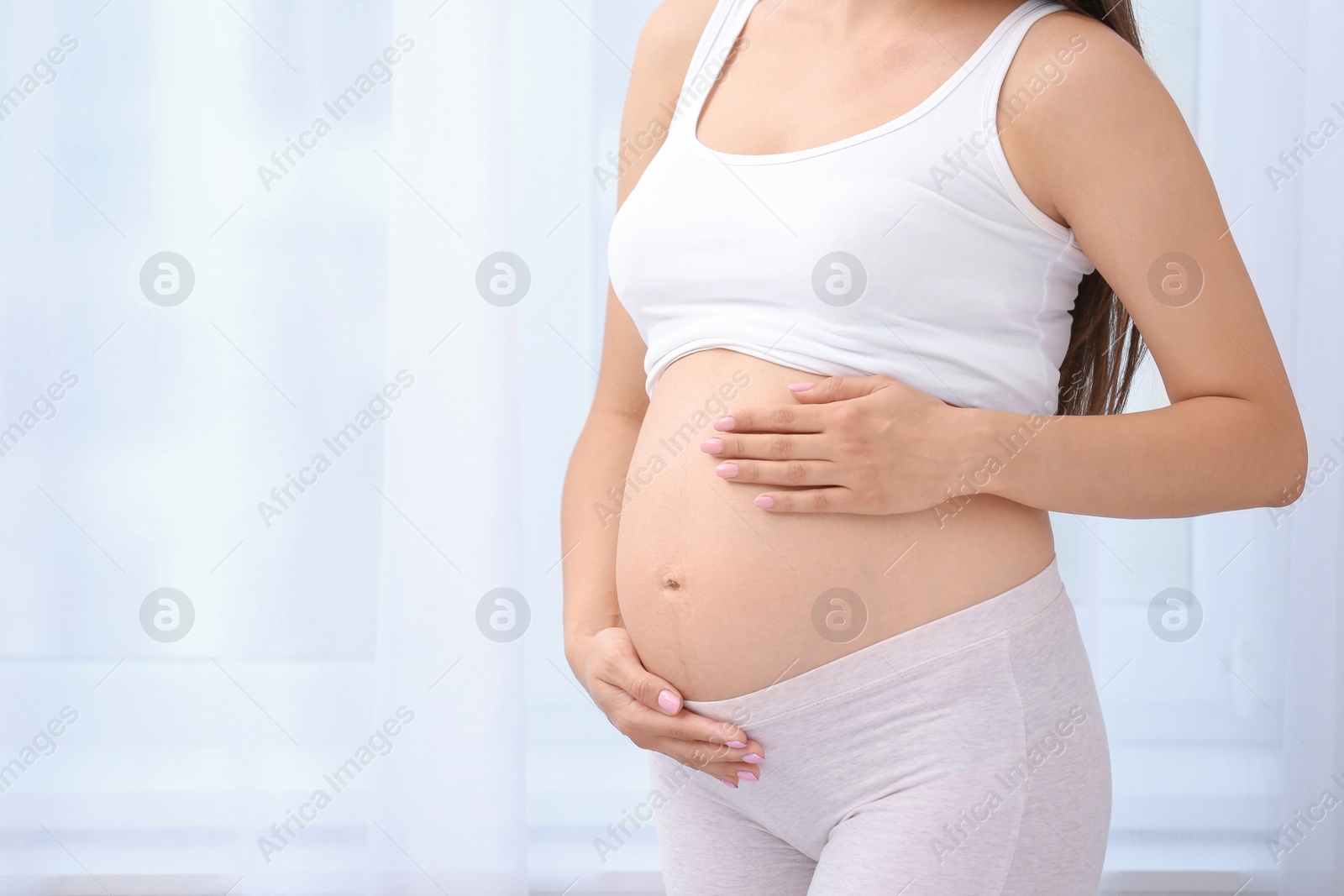 Photo of Young pregnant woman near window at home, closeup