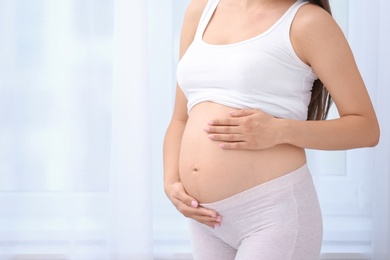 Photo of Young pregnant woman near window at home, closeup