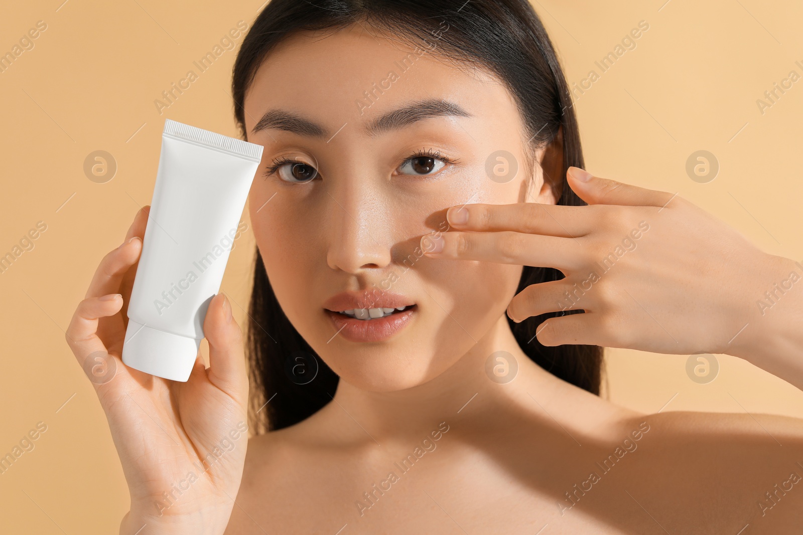 Photo of Beautiful young woman holding sun protection cream on beige background, closeup