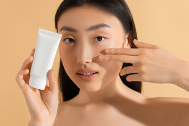 Beautiful young woman holding sun protection cream on beige background, closeup