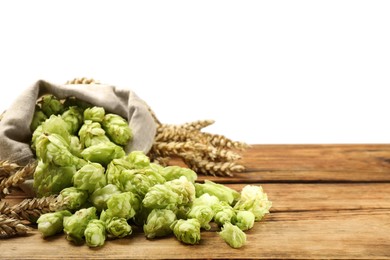Photo of Overturned sack of hop flowers and wheat ears on wooden table against white background, space for text