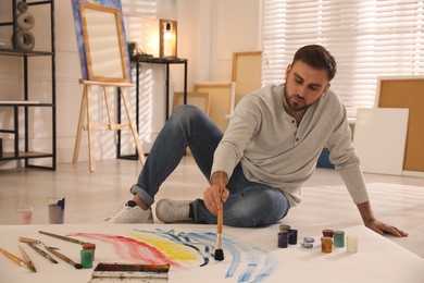 Photo of Young man painting on canvas with brush in artist studio