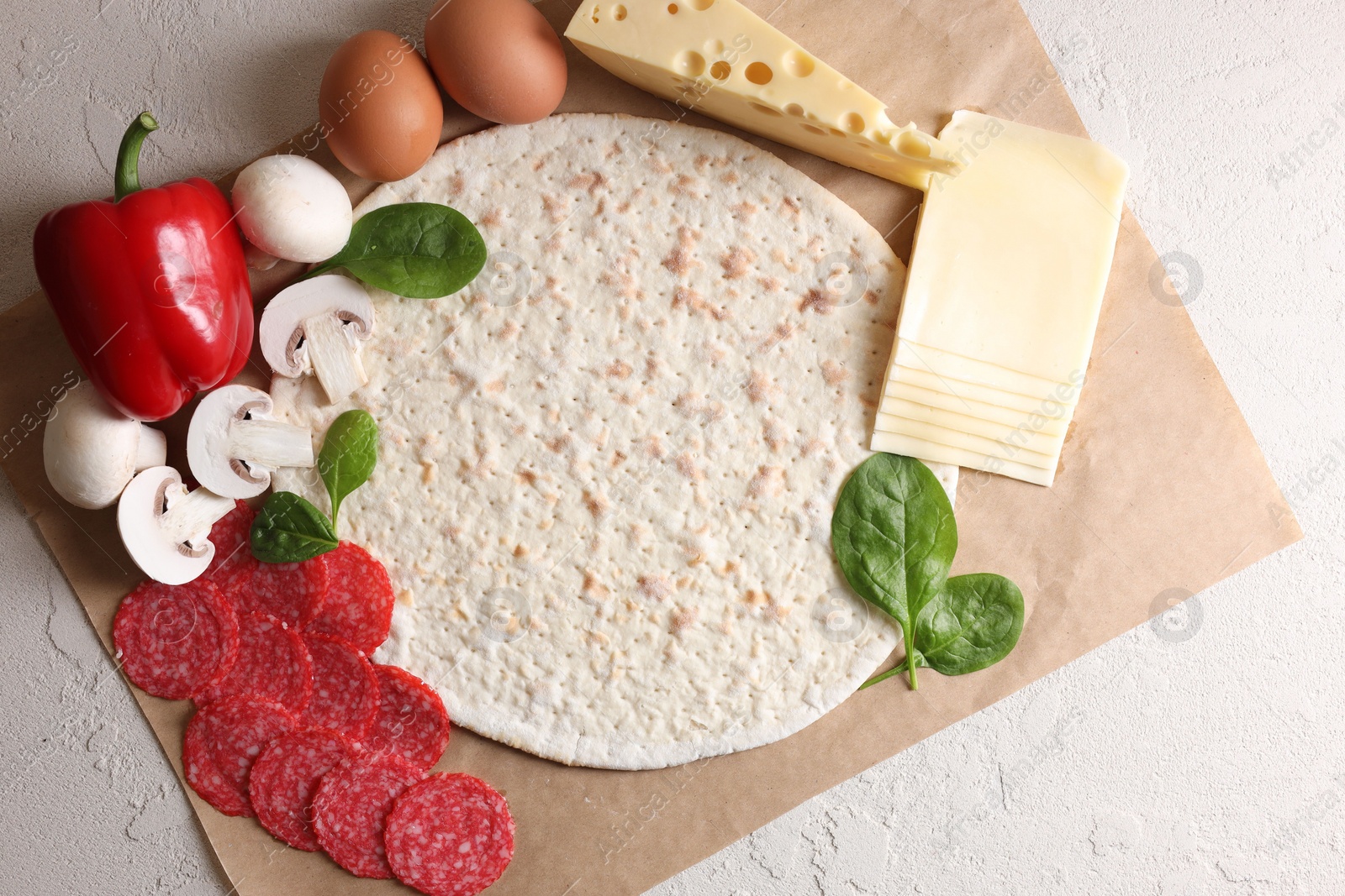 Photo of Pizza base and products on light textured table, top view