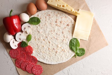 Pizza base and products on light textured table, top view