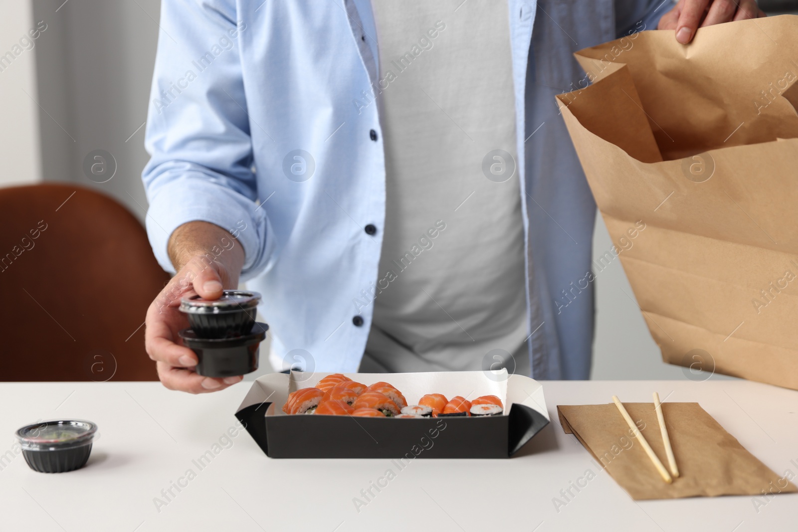 Photo of Man unpacking his order from sushi restaurant at table in room, closeup