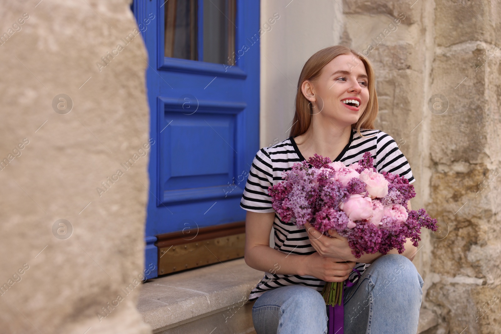 Photo of Beautiful woman with bouquet of spring flowers near building outdoors, space for text