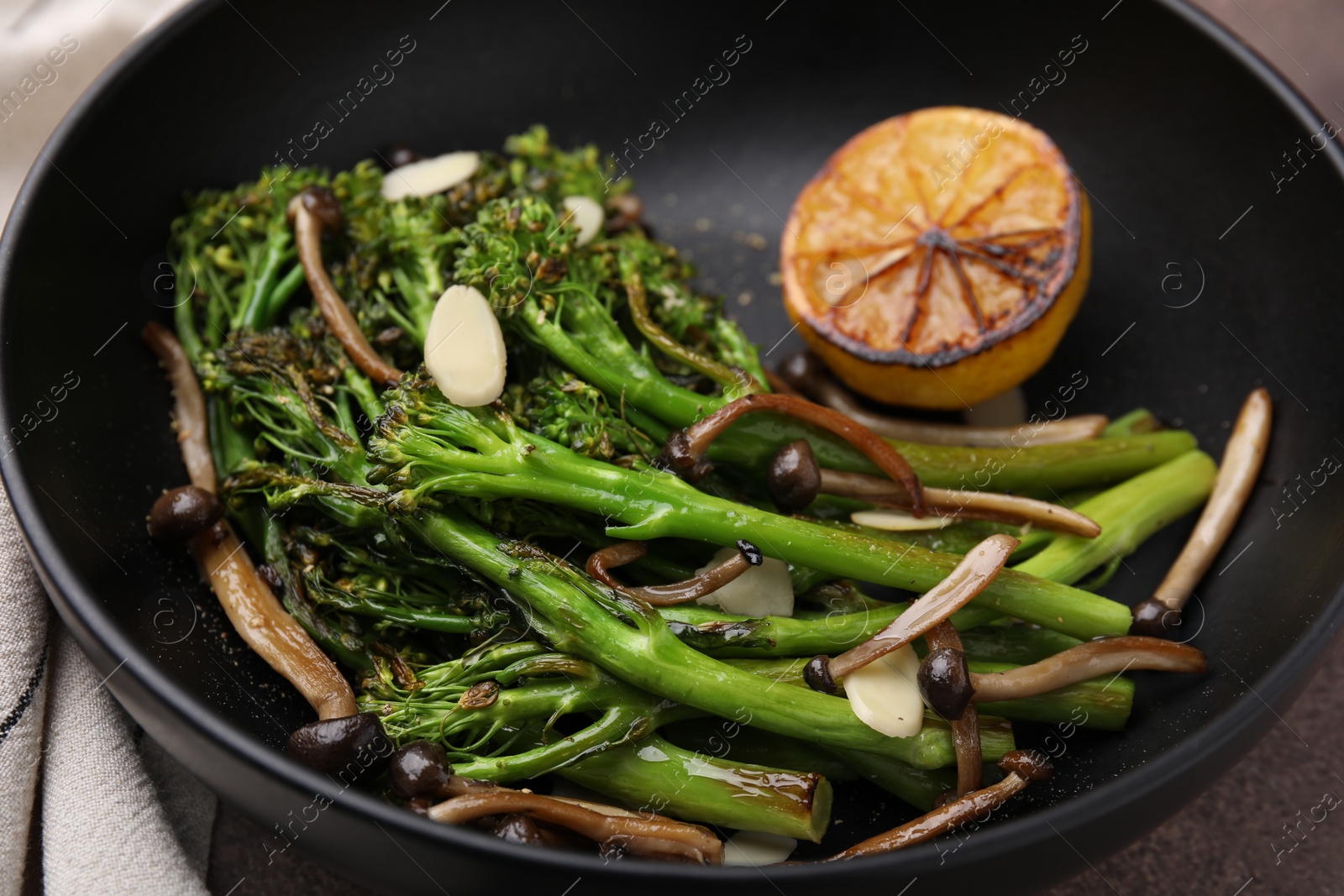Photo of Tasty cooked broccolini with lemon and mushrooms in bowl, closeup