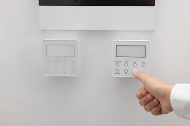 Photo of Woman adjusting thermostat on white wall, closeup. Smart home system