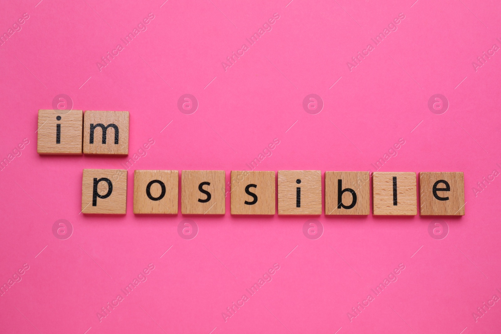 Photo of Motivation concept. Changing word from Impossible into Possible by removing wooden square with letters I and M on pink background, top view