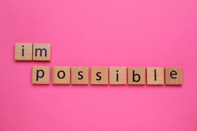 Motivation concept. Changing word from Impossible into Possible by removing wooden square with letters I and M on pink background, top view