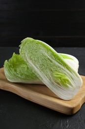 Photo of Whole and cut fresh Chinese cabbages on black textured table