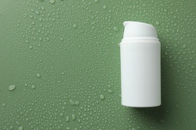 Moisturizing cream in bottle on green background with water drops, top view. Space for text