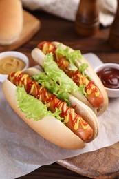 Photo of Tasty hot dogs with lettuce, ketchup and mustard on table