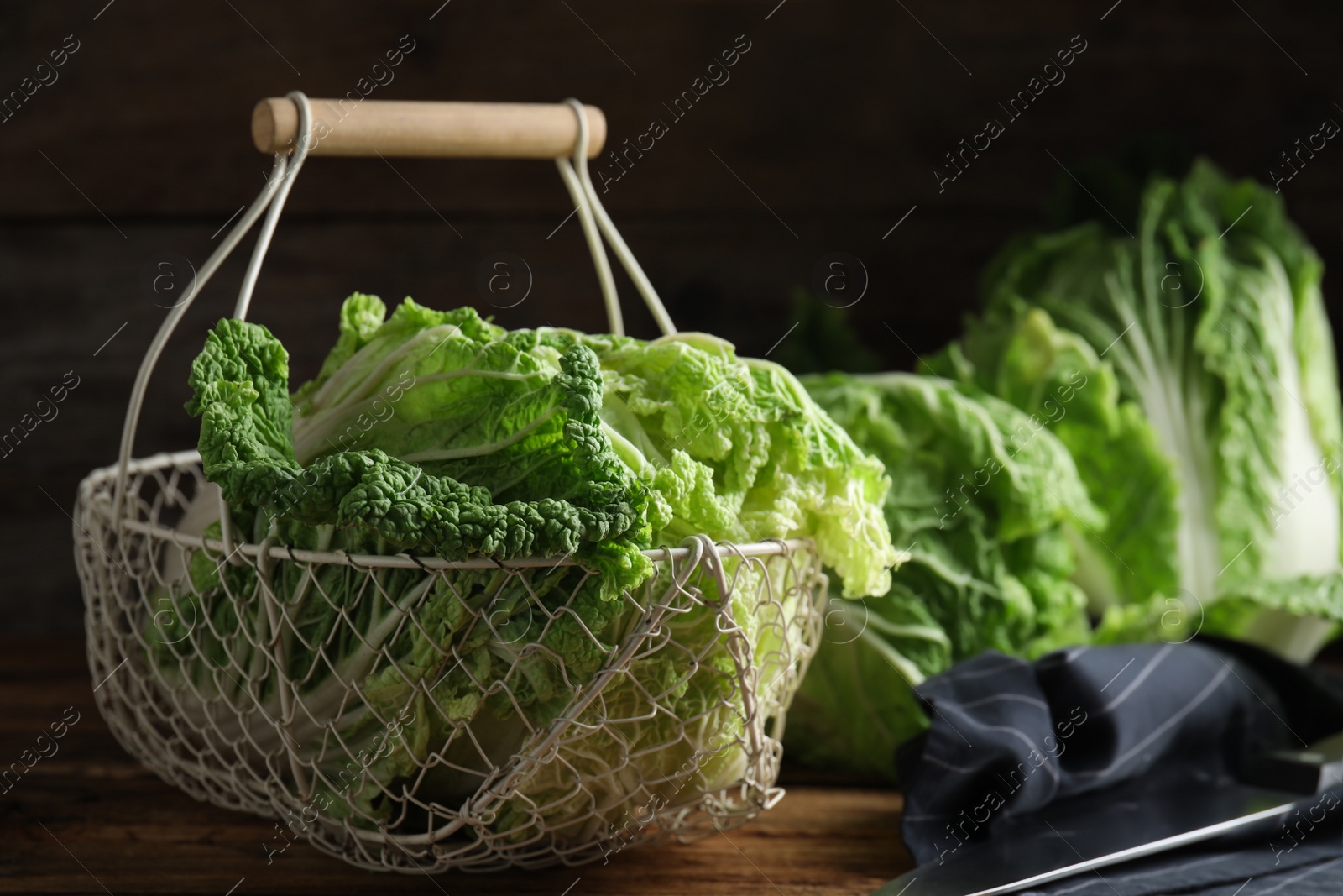 Photo of Ripe Chinese cabbages in metal basket on wooden table