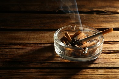 Smoldering cigarette in glass ashtray on wooden table. Space for text