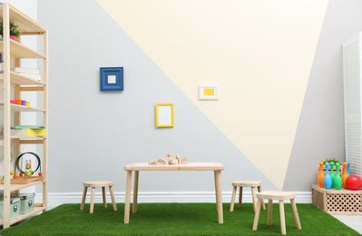 Stylish playroom interior with table, stools and green carpet