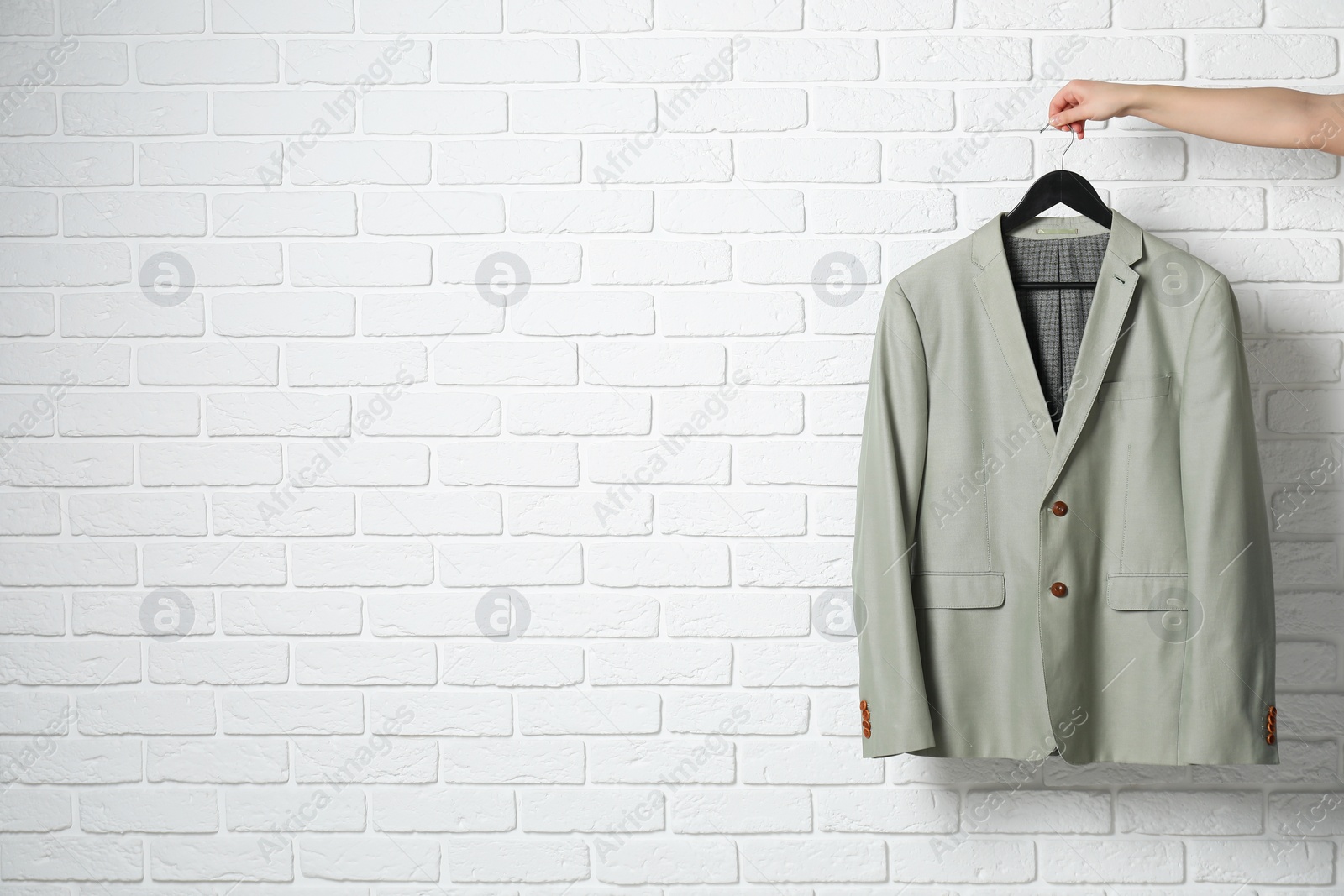 Photo of Woman holding hanger with grey jacket near white brick wall, closeup. Space for text