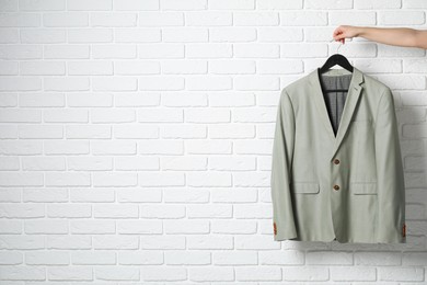 Photo of Woman holding hanger with grey jacket near white brick wall, closeup. Space for text