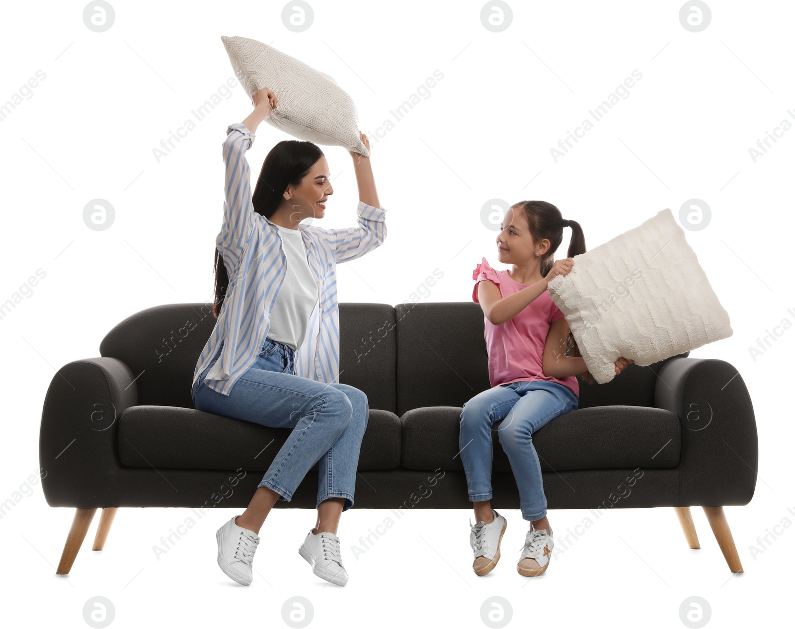 Photo of Young woman and her daughter having pillow fight on comfortable grey sofa against white background