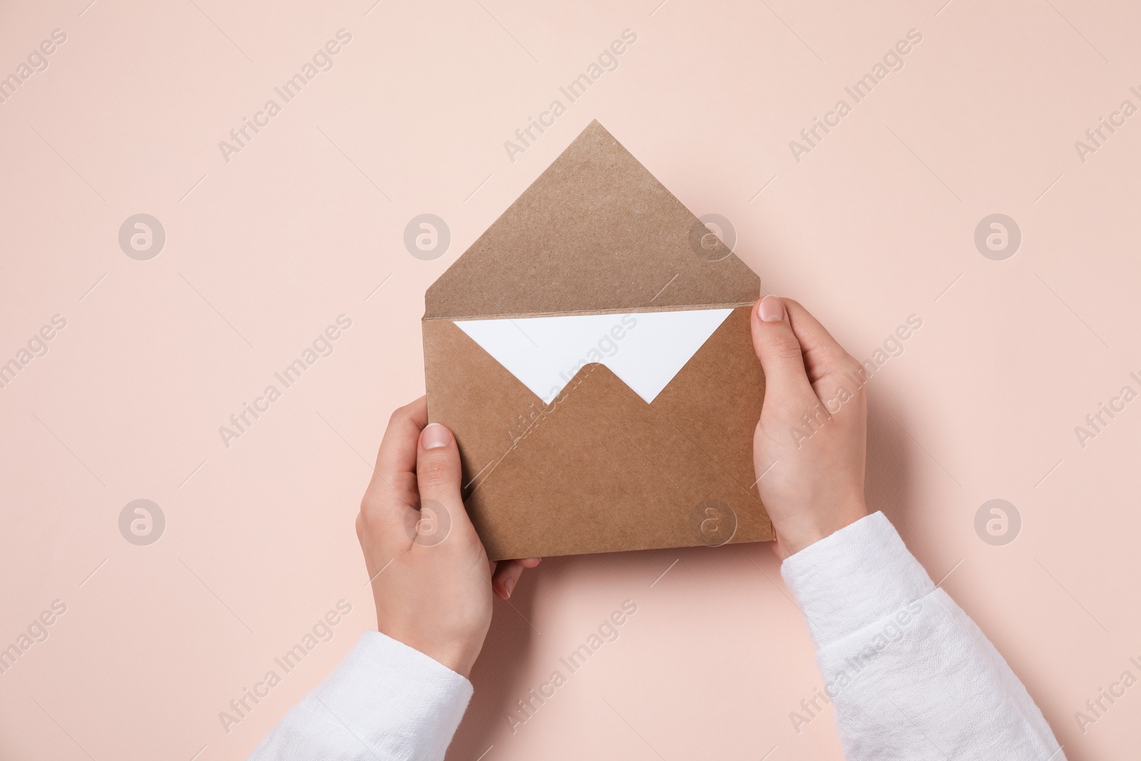 Photo of Woman holding letter envelope with card at beige table, top view