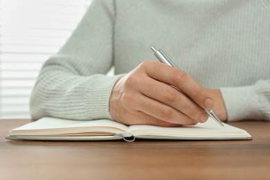 Man writing in notebook at wooden table, closeup