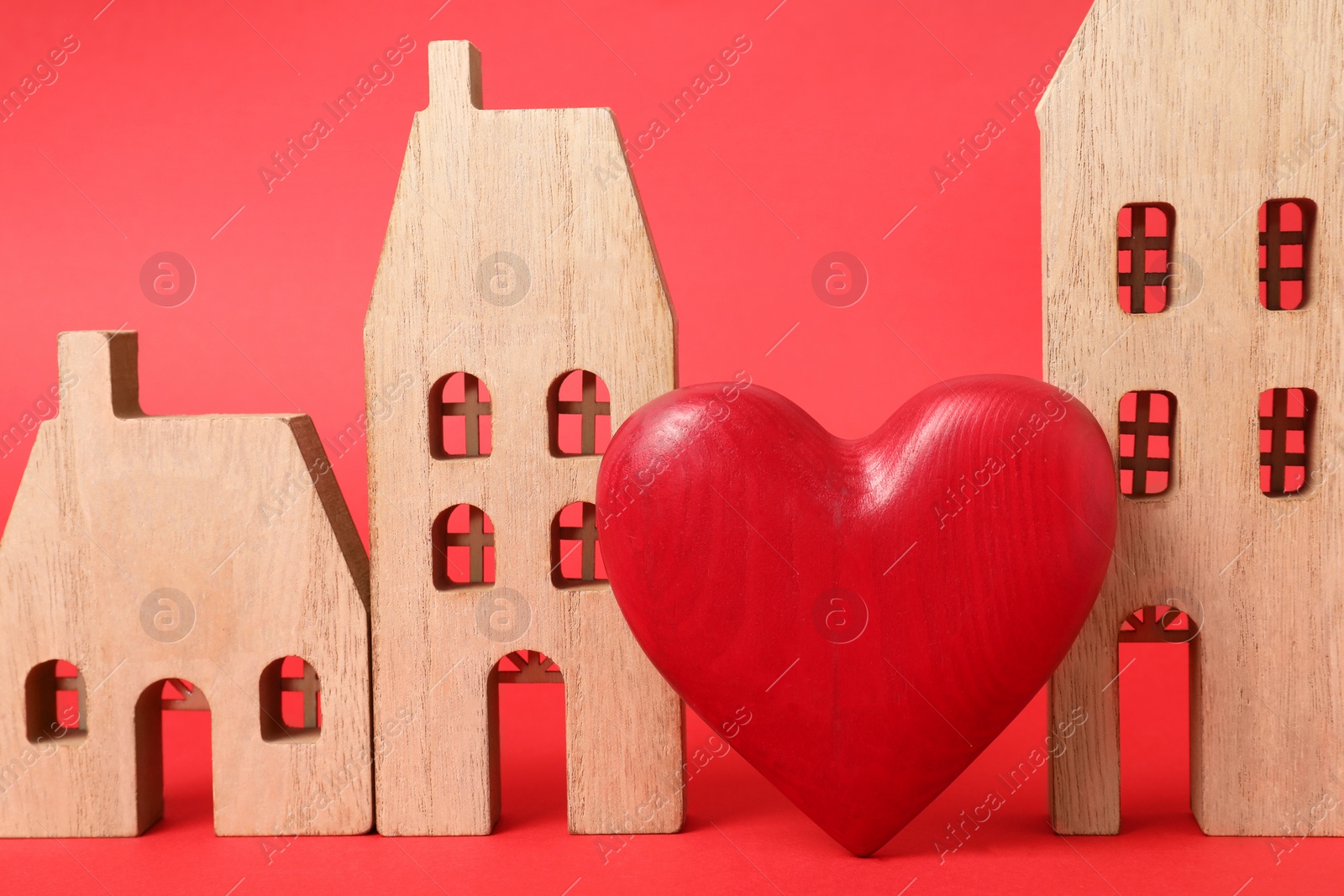 Photo of Long-distance relationship concept. Wooden house models and decorative heart on red background, closeup