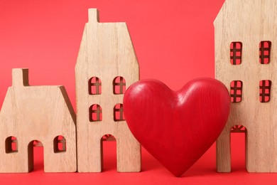 Photo of Long-distance relationship concept. Wooden house models and decorative heart on red background, closeup