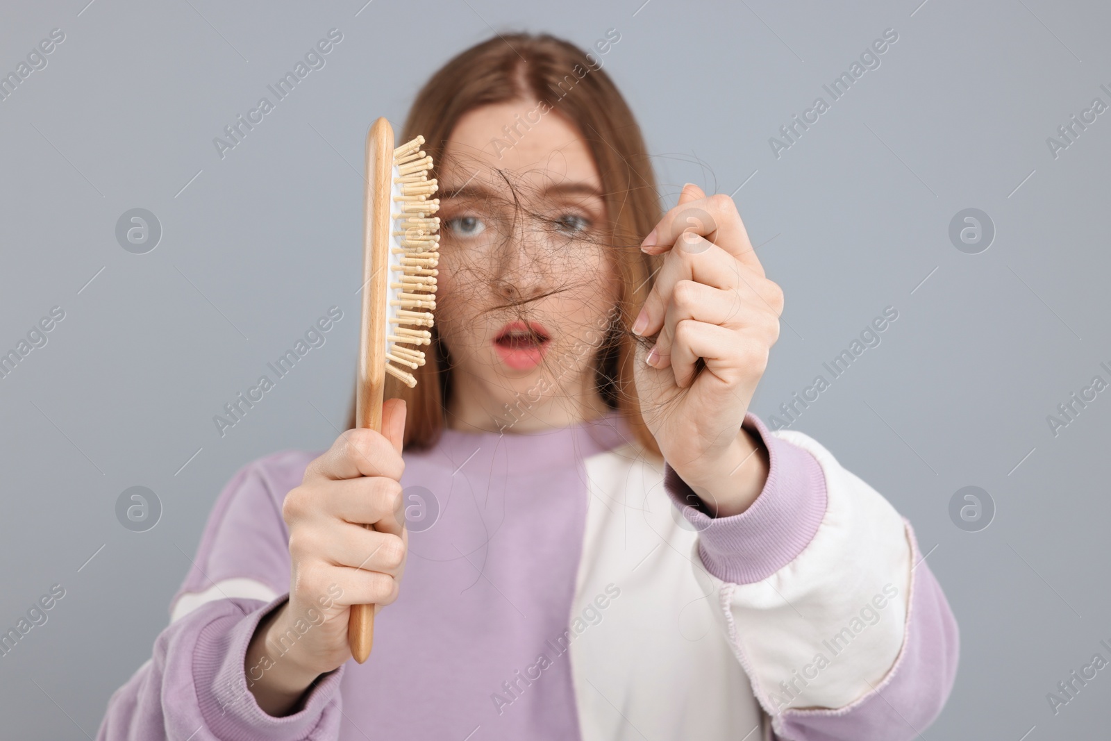 Photo of Woman untangling her lost hair from brush on light grey background, selective focus. Alopecia problem